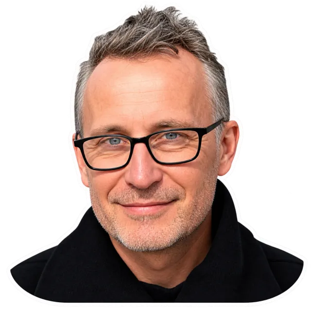 Portrait de Patrick Stefan Rheinert, souriant, lunettes à monture noire et manteau sombre