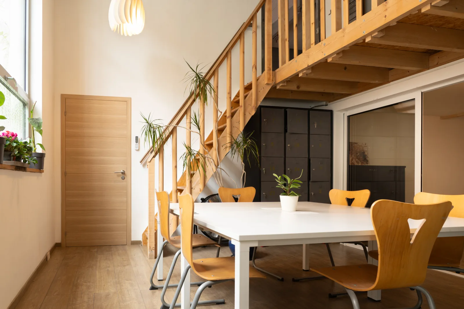 Bureau partagé de la grünboX : grande table blanche, chaises en bois clair et escalier en bois sous une mezzanine
