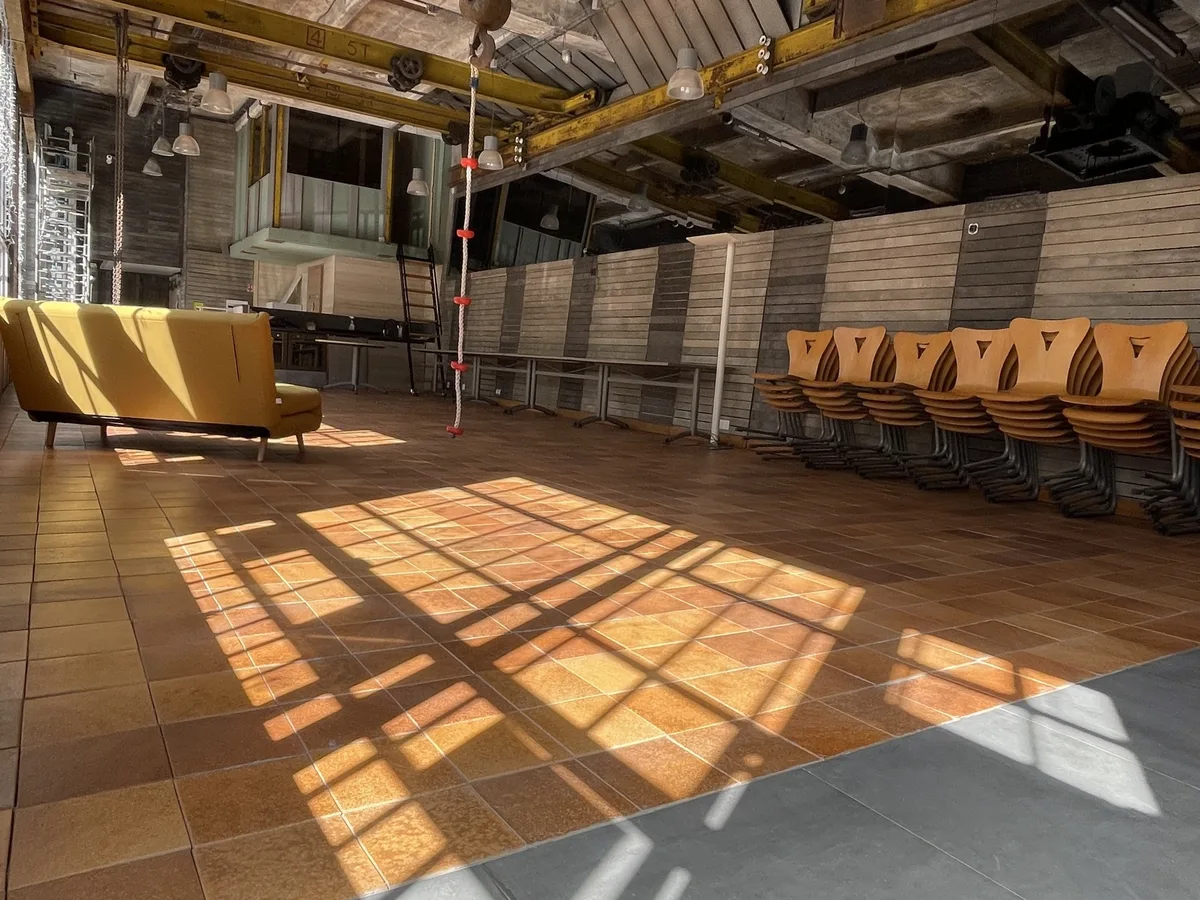 Grande salle de la grünboX baignée de soleil, chaises alignées le long du mur